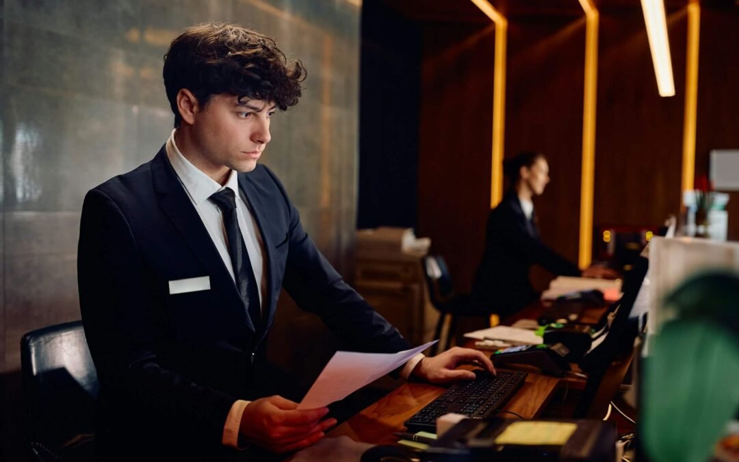 Male receptionist working on desktop PC at hotel front desk.